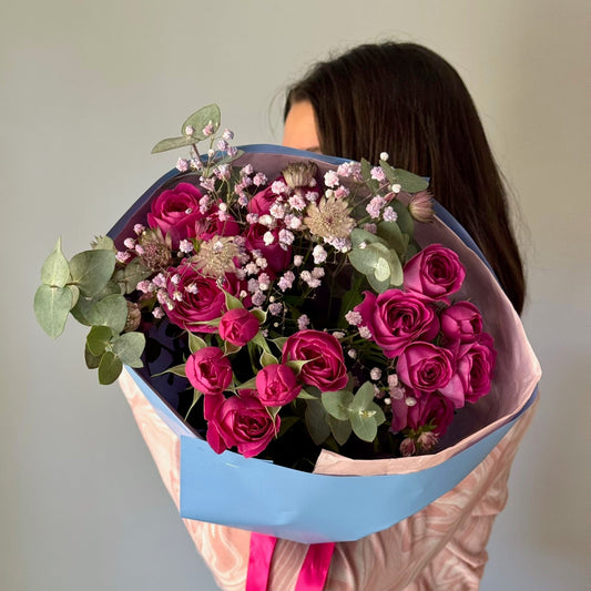 Person holding a bouquet of pink and purple flowers with a plain background