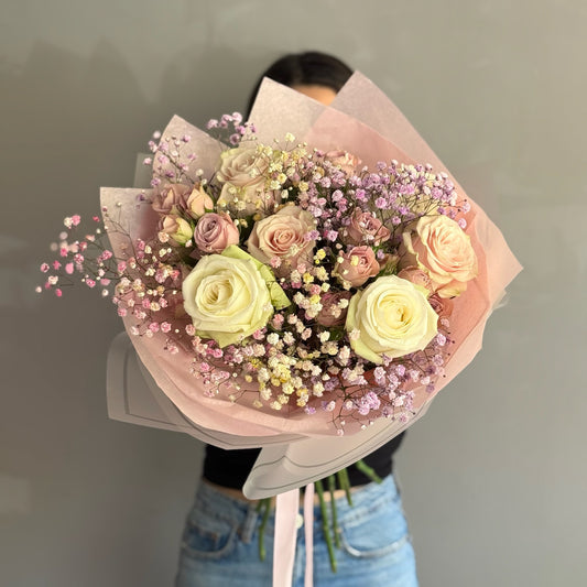 Bouquet of pink, white, and beige roses with small blue flowers held by a person.