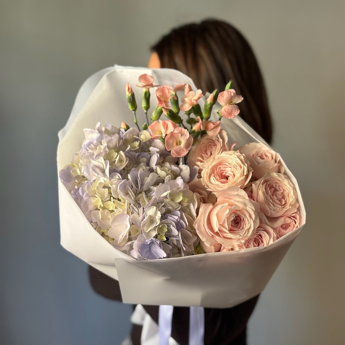 Person holding a bouquet of flowers wrapped in white paper against a blurred background
