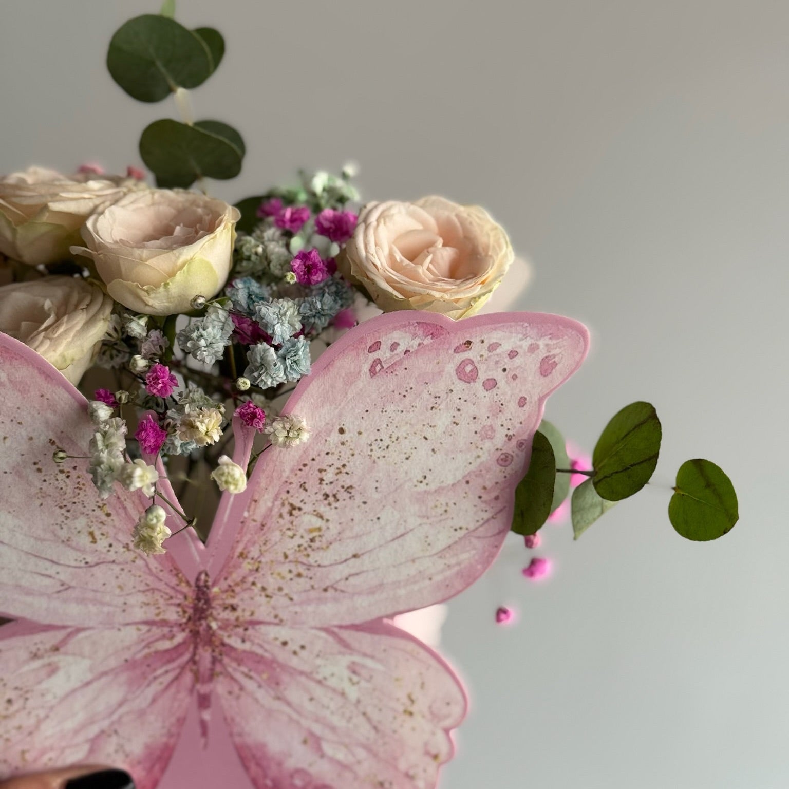 Bouquet of flowers with a pink butterfly decoration against a light gray background