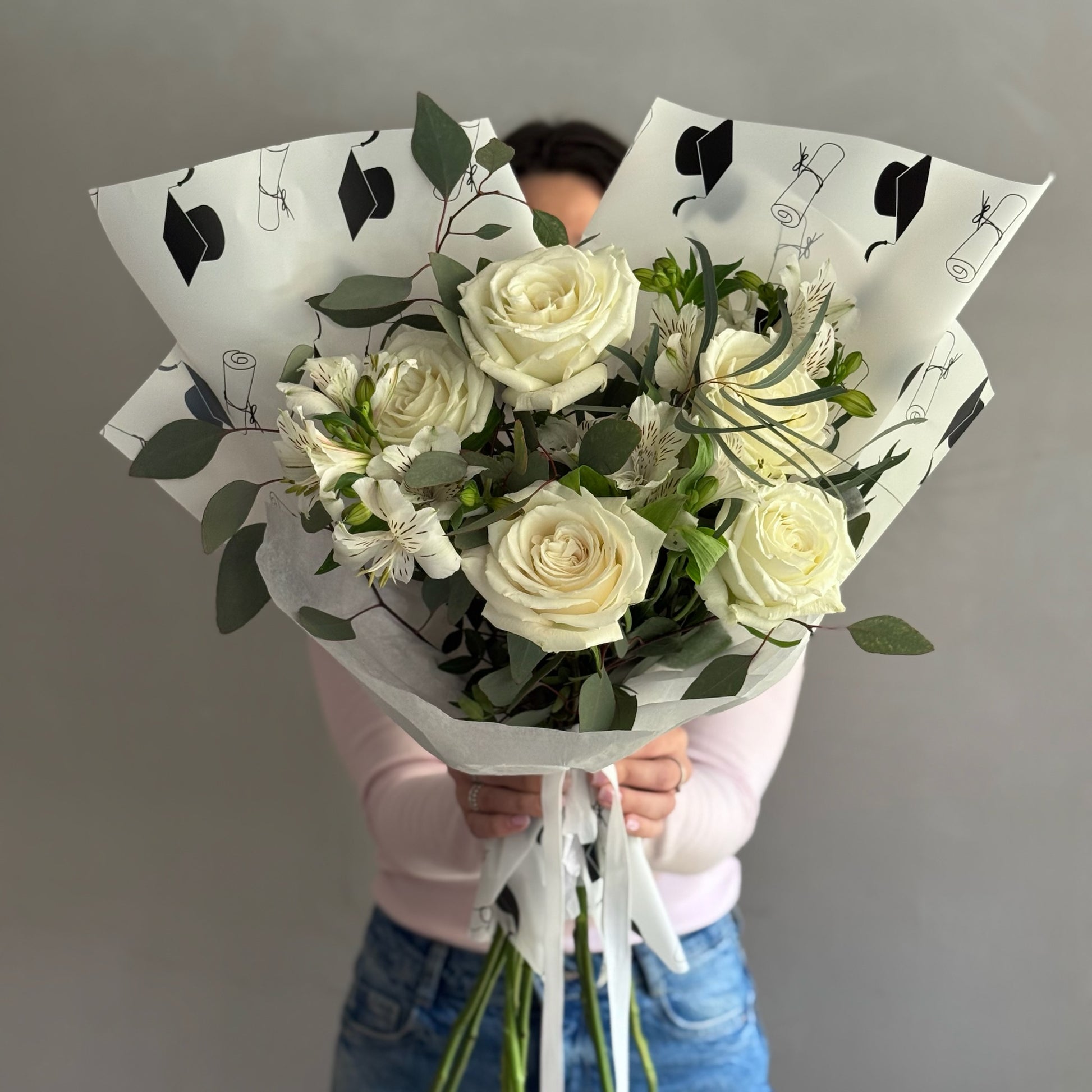 Graduation wrapping bouquet with white flowers held by person on grey background 