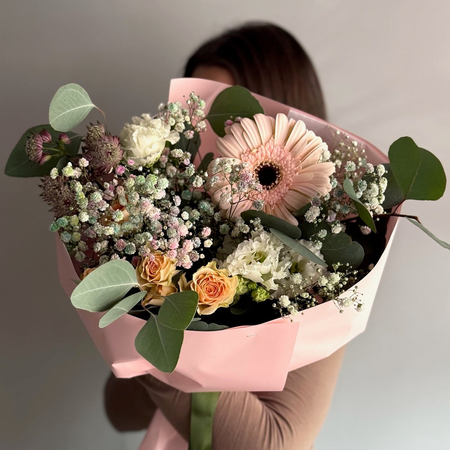 Person holding a bouquet of flowers wrapped in pink paper against a neutral background