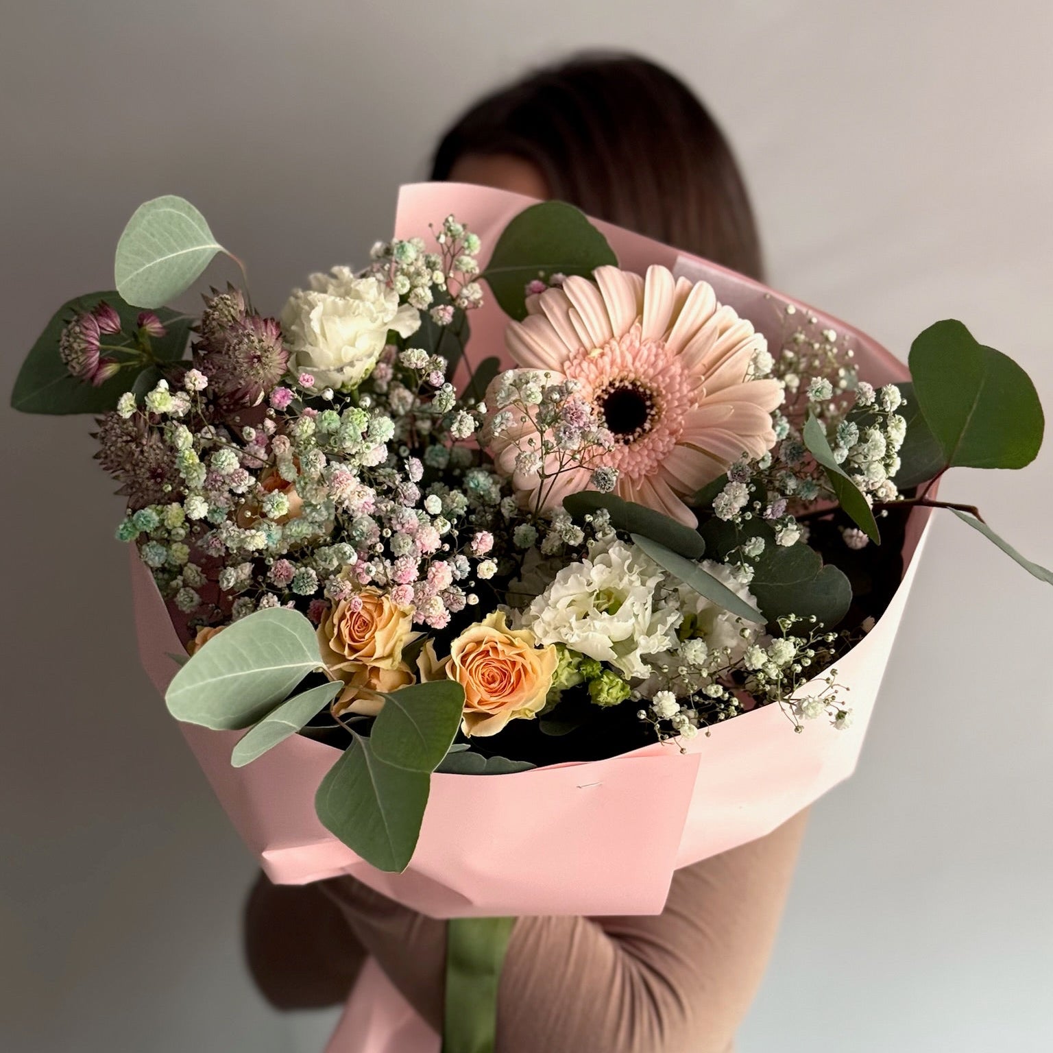 Person holding a bouquet of flowers wrapped in pink paper against a neutral background