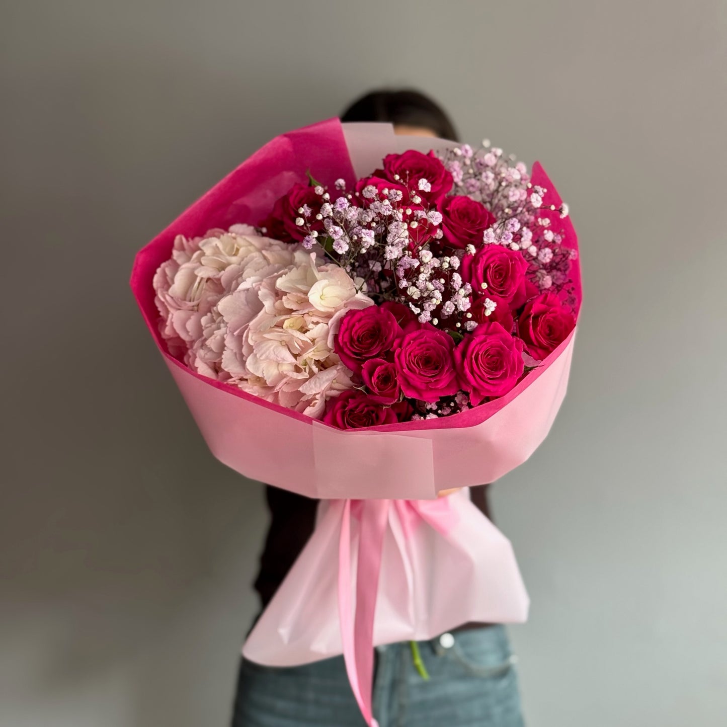 Person holding a large bouquet of pink and red flowers with a blurred background