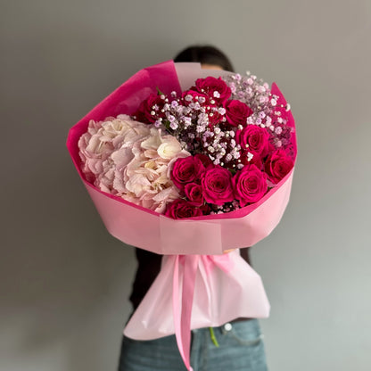 Person holding a large bouquet of pink and red flowers with a blurred background