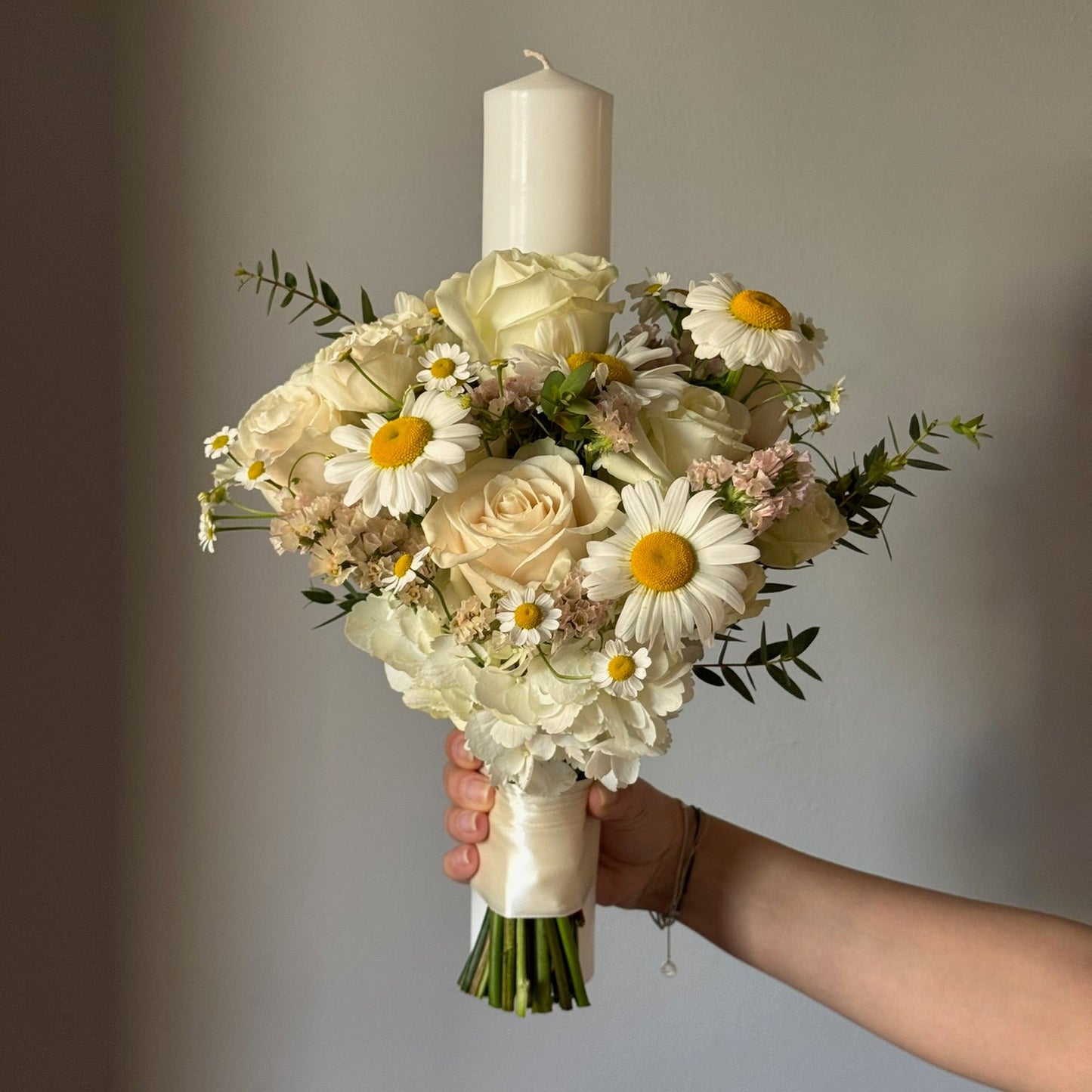 Candle with bouquet of flowers held on grey background 