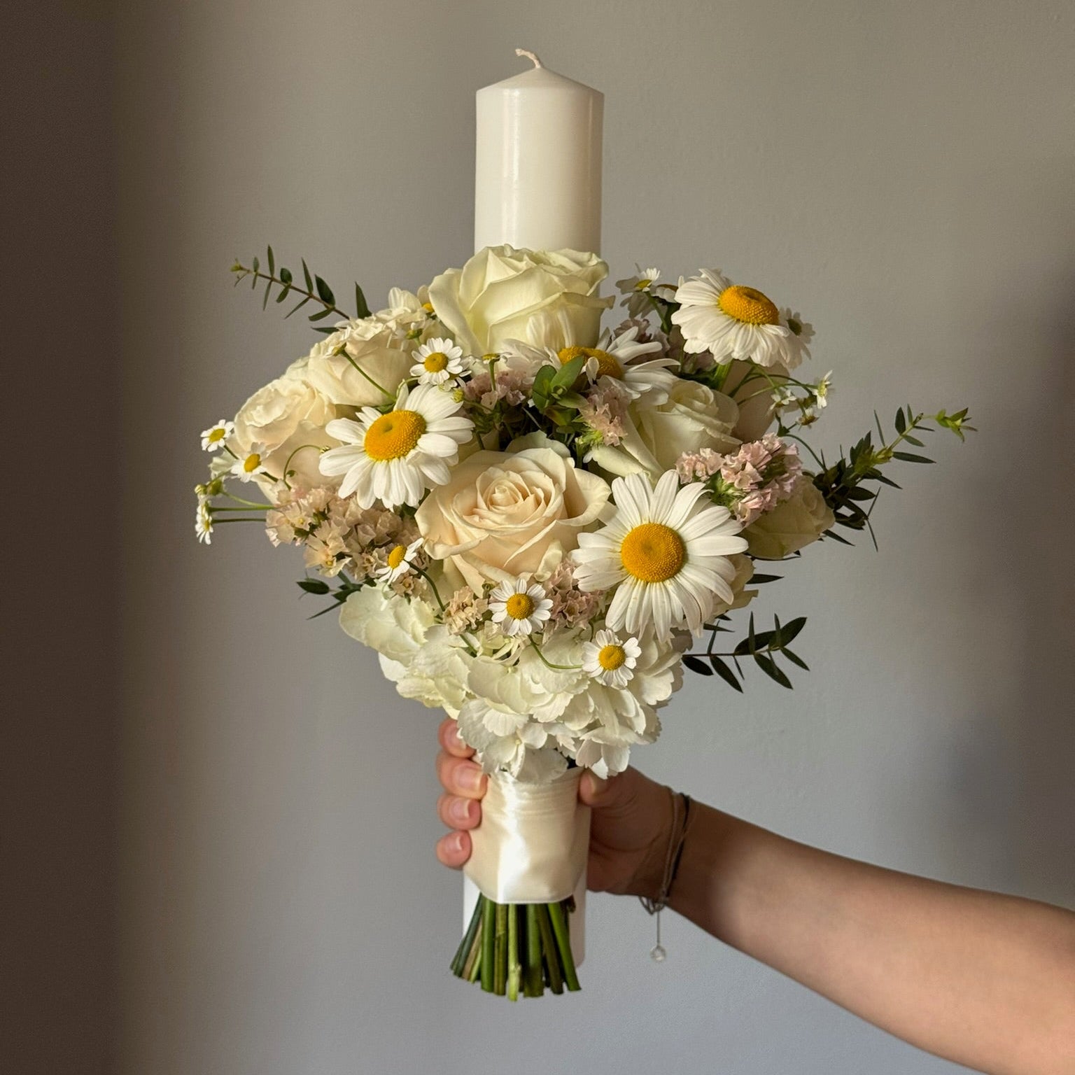 Candle with bouquet of flowers held on grey background 