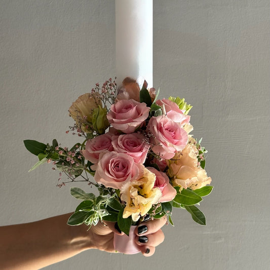 Hand holding a bouquet of pink and yellow flowers against a plain background