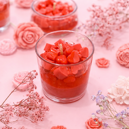 Red heart-shaped candles in glass containers on a pink floral background