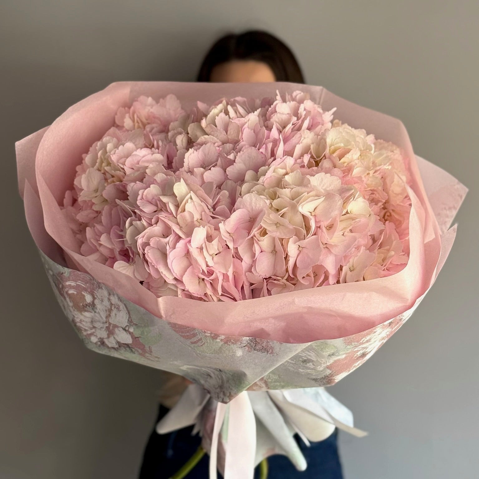 Person holding pink big bouquet at grey background 