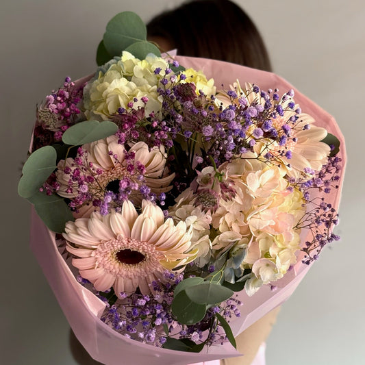 Bouquet of flowers wrapped in pink paper held by a person against a neutral background
