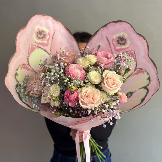 Pink bouquet with pink flowers and butterfly wrapping paper held by person on grey background 