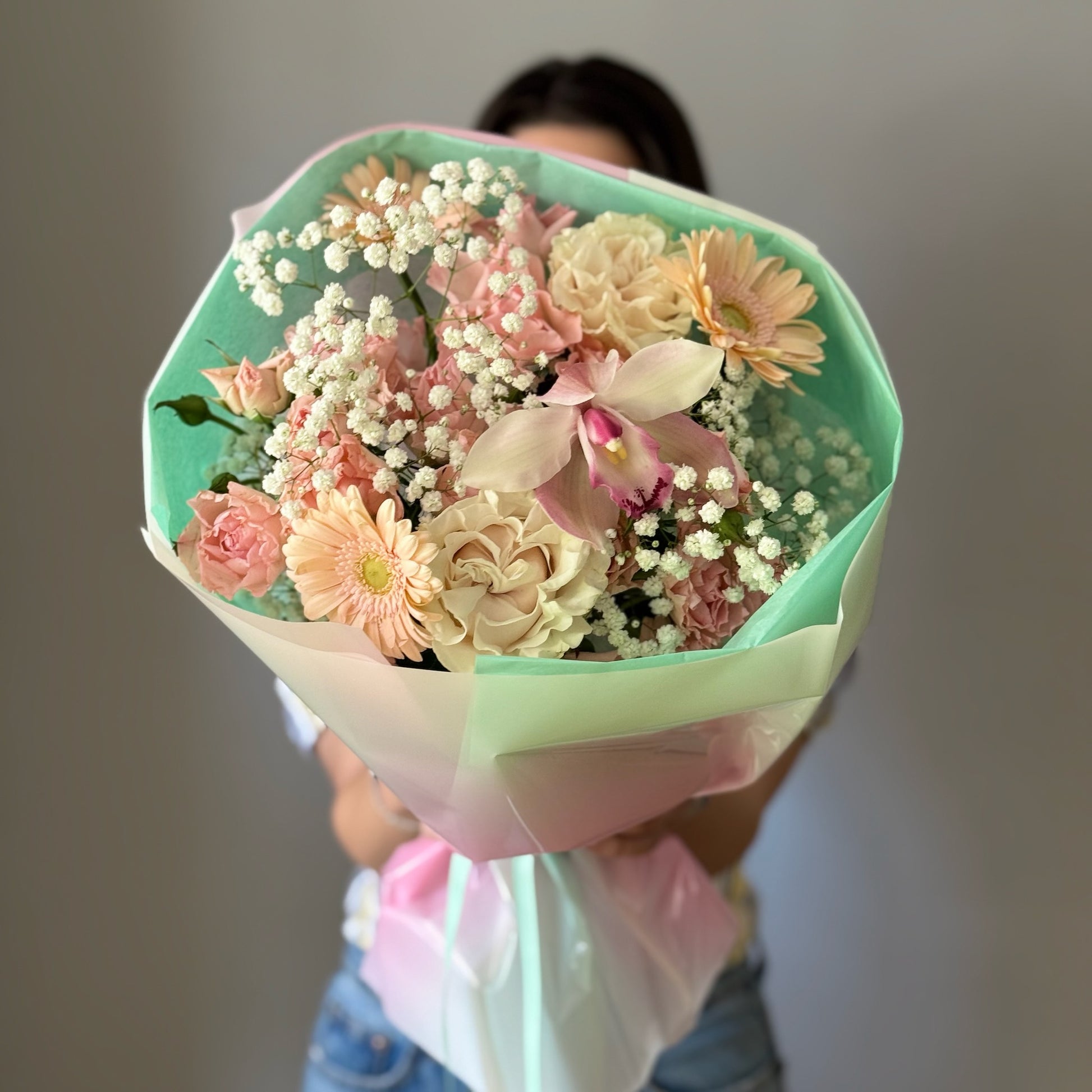 White and pink flowers wrapped in a bouquet held by person on grey background 