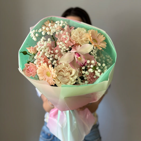 White and pink flowers wrapped in a bouquet held by person on grey background 