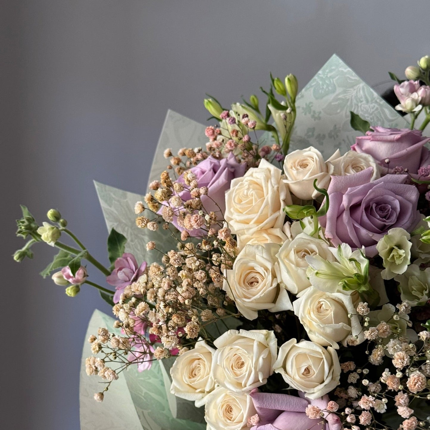 Bouquet of white and purple roses with greenery on a gray background