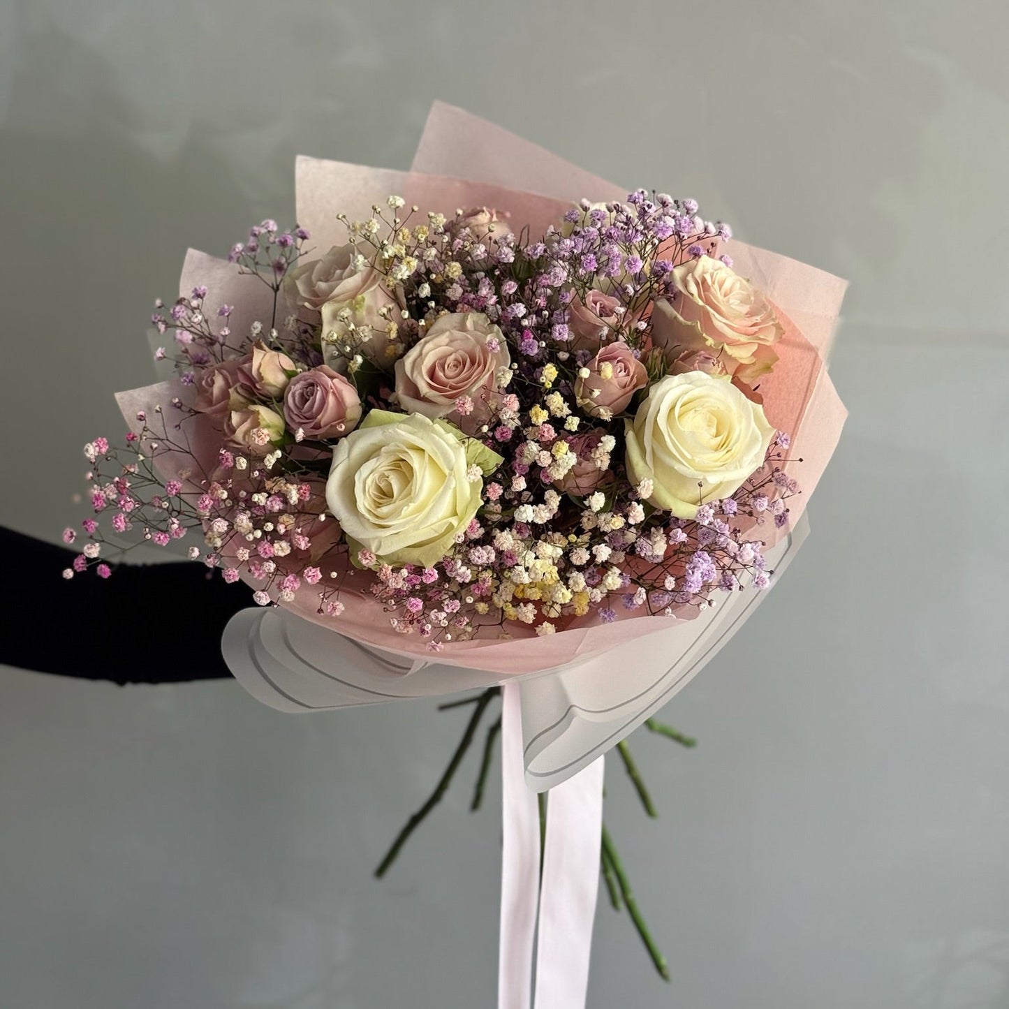 Bouquet of pink, white, and beige roses with small blue flowers held by a person.