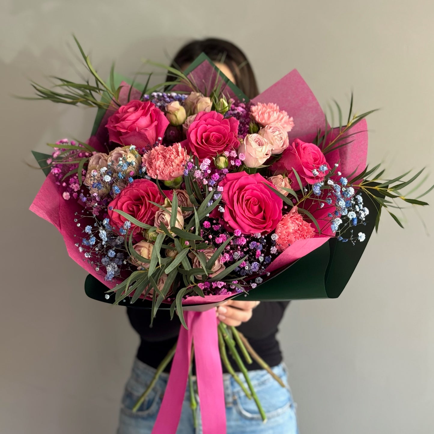 Pink fucsia bouquet with greenery held by person on grey background 