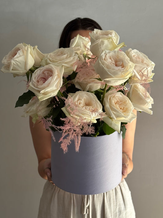 Person holding a large bouquet of white and pink roses in a gray box against a plain background