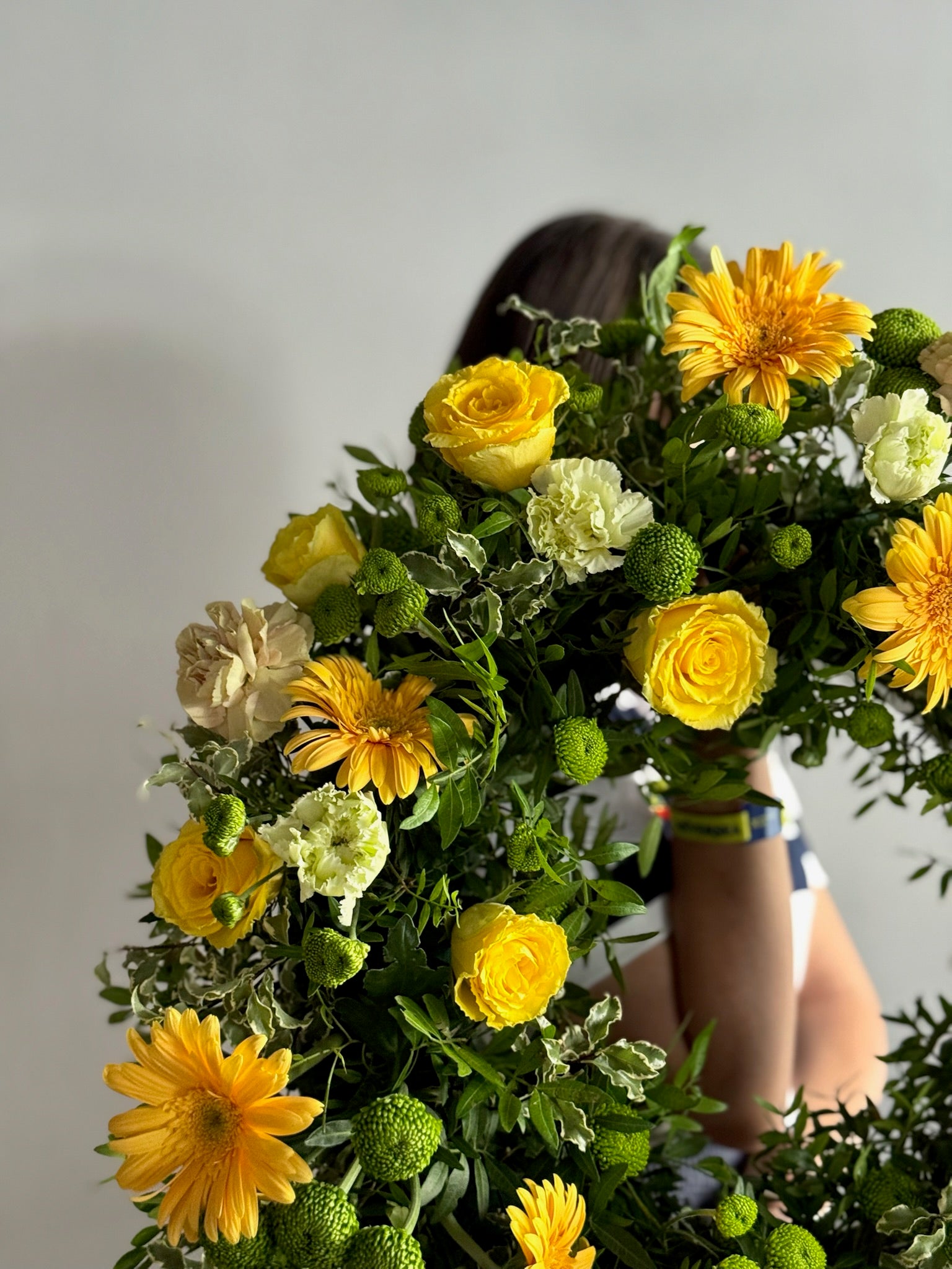 Person holding a large bouquet of yellow and white flowers against a neutral background