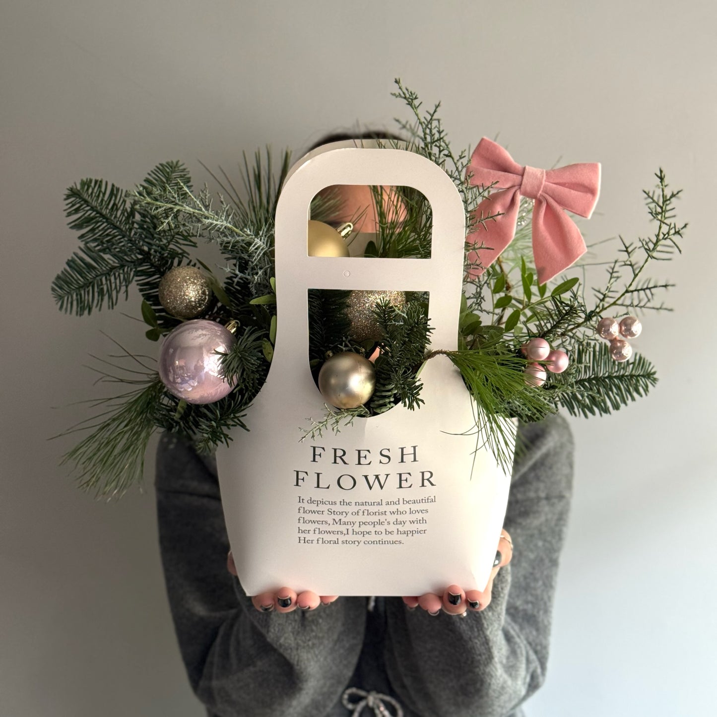 Person holding a white bag labeled 'Fresh Flower' with decorative greenery and ornaments.