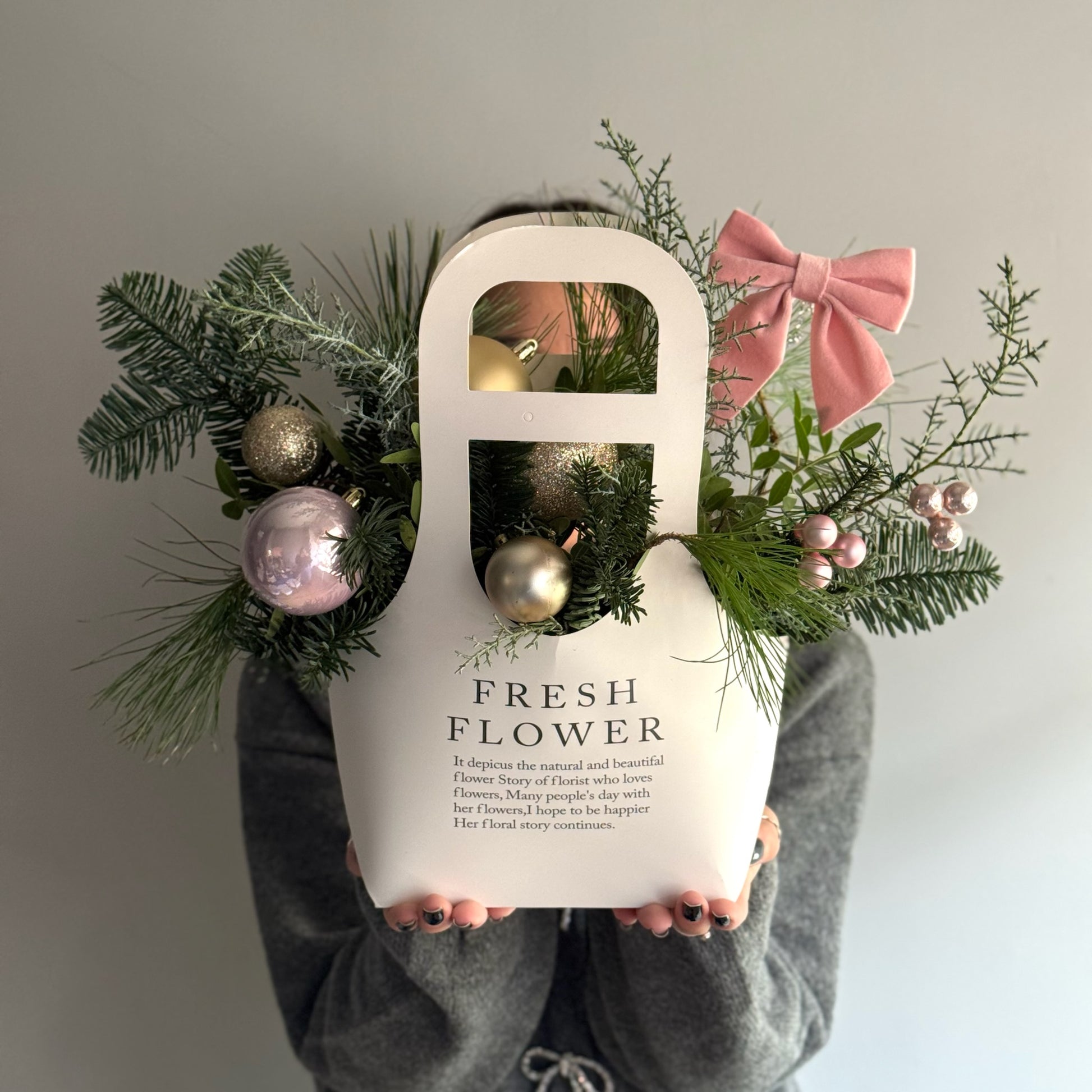 Person holding a white bag labeled 'Fresh Flower' with decorative greenery and ornaments.
