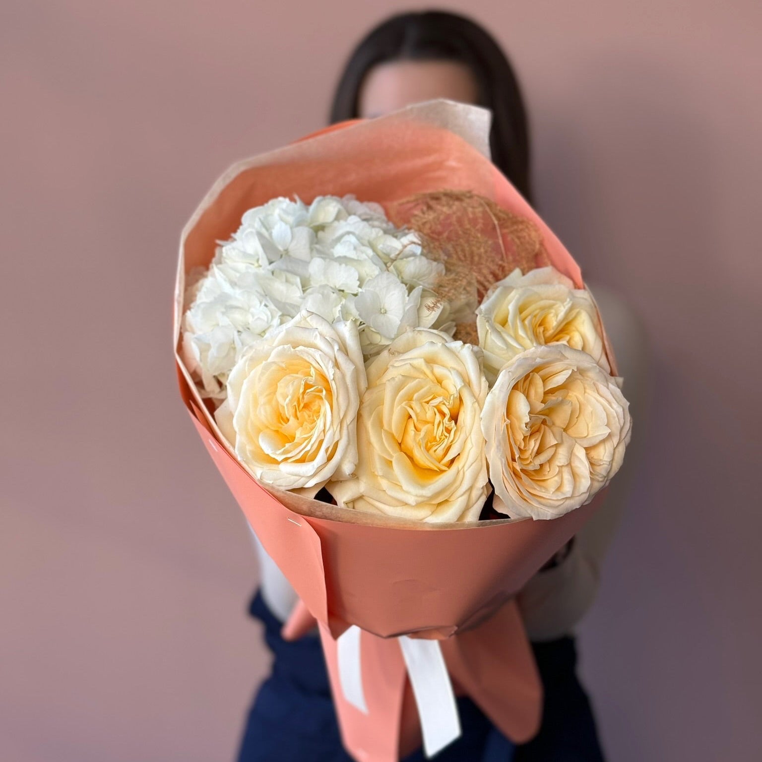 Bouquet of white and yellow roses wrapped in brown paper held by a person against a blurred background