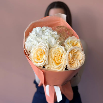 Bouquet of white and yellow roses wrapped in brown paper held by a person against a blurred background