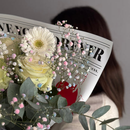 Person holding a bouquet of flowers with a blurred face, wearing a white coat with red floral patterns.