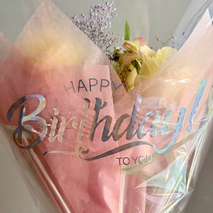 Bouquet of flowers wrapped in pink paper with 'Happy Birthday To You' text on a white background