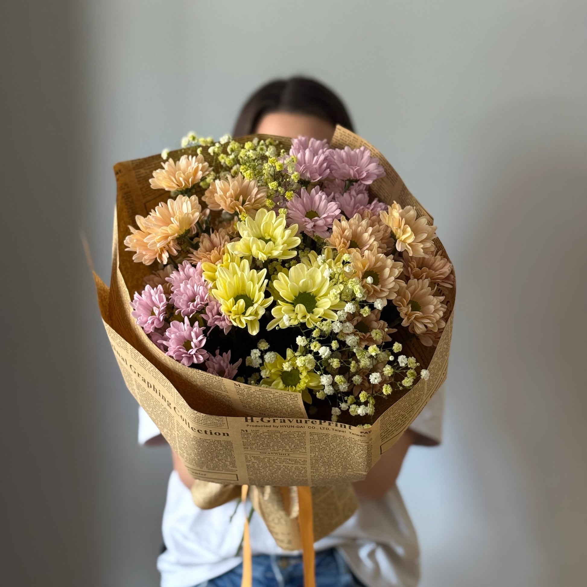 Colorful flowers in newspaper wrapping paper in bouquet on grey background 