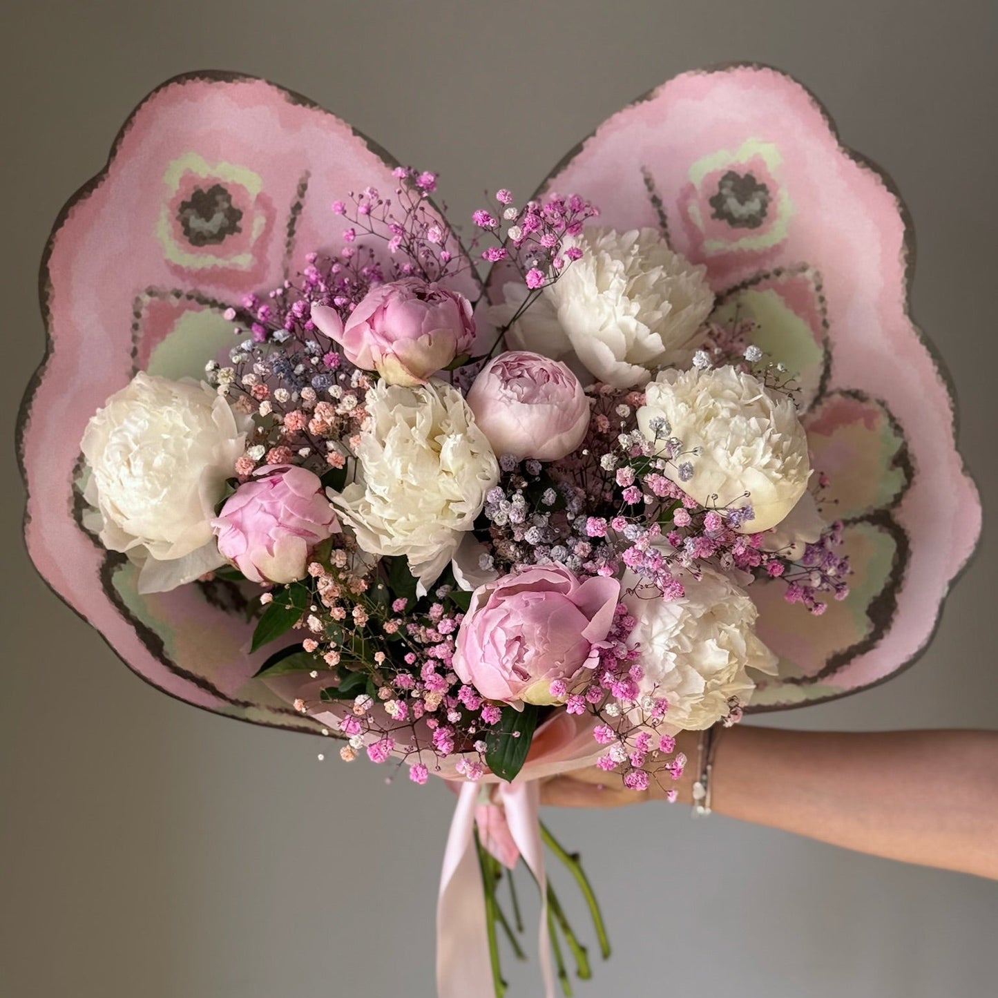 White and pink flowers in butterfly bouquet held on grey background 