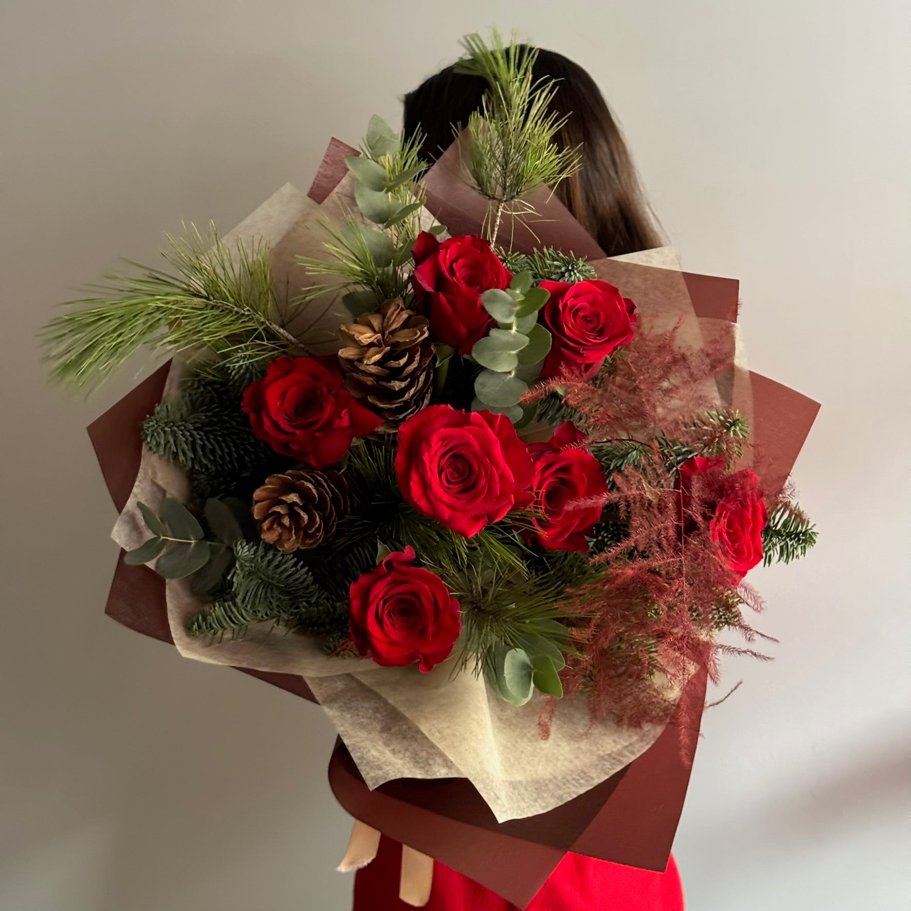 Bouquet of red roses with greenery held by a person wearing a red dress.