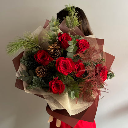 Bouquet of red roses with greenery held by a person wearing a red dress.