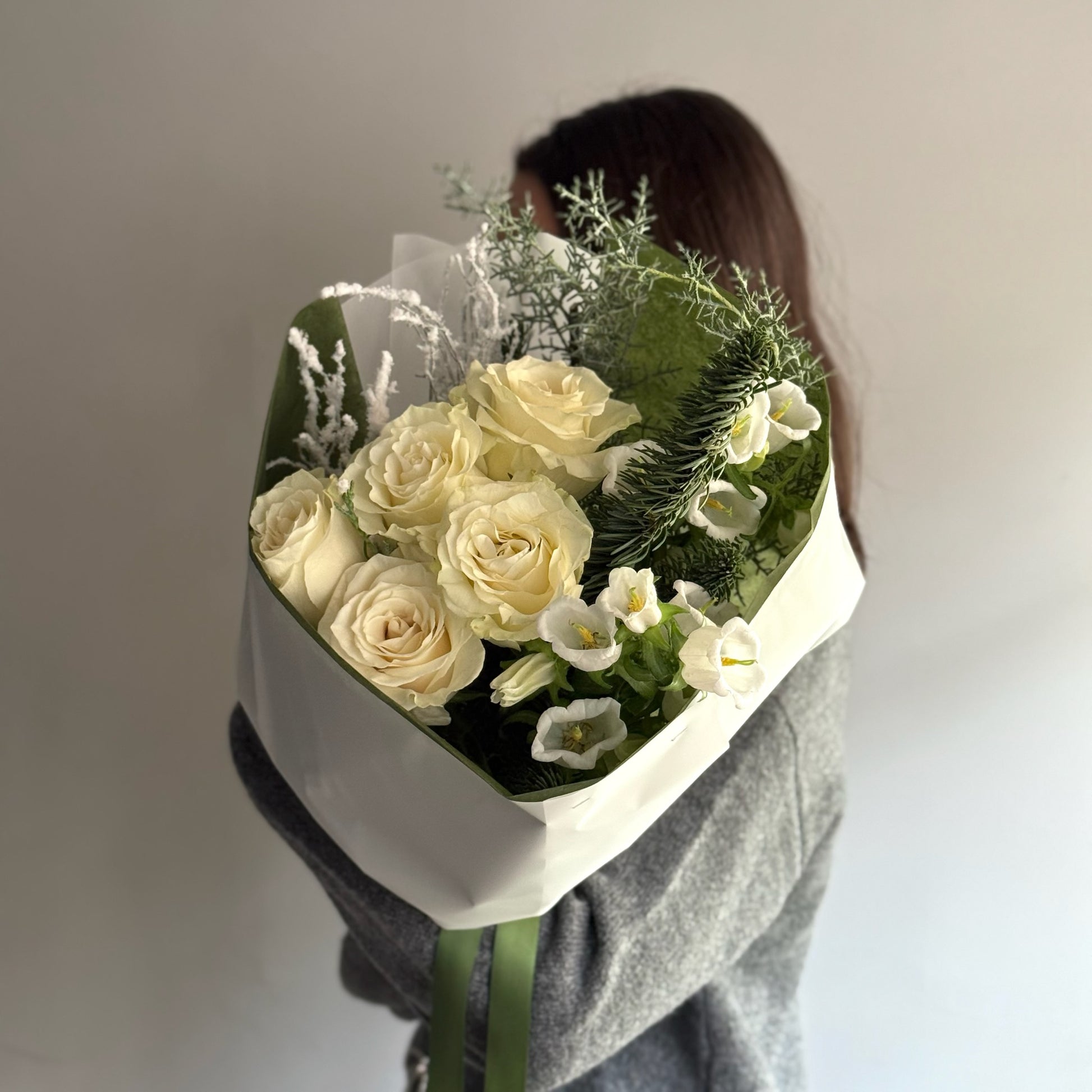 Person holding a bouquet of white roses and greenery against a plain background