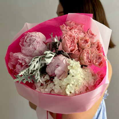 Pink flowers in a round bouquet held by person on grey background 