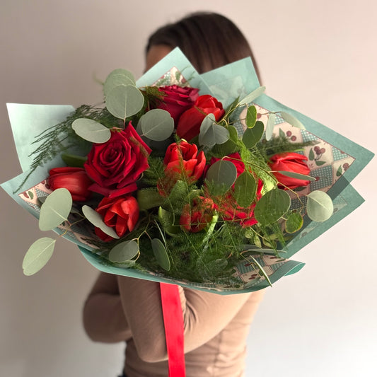 Bouquet of red roses with greenery held by a person against a neutral background