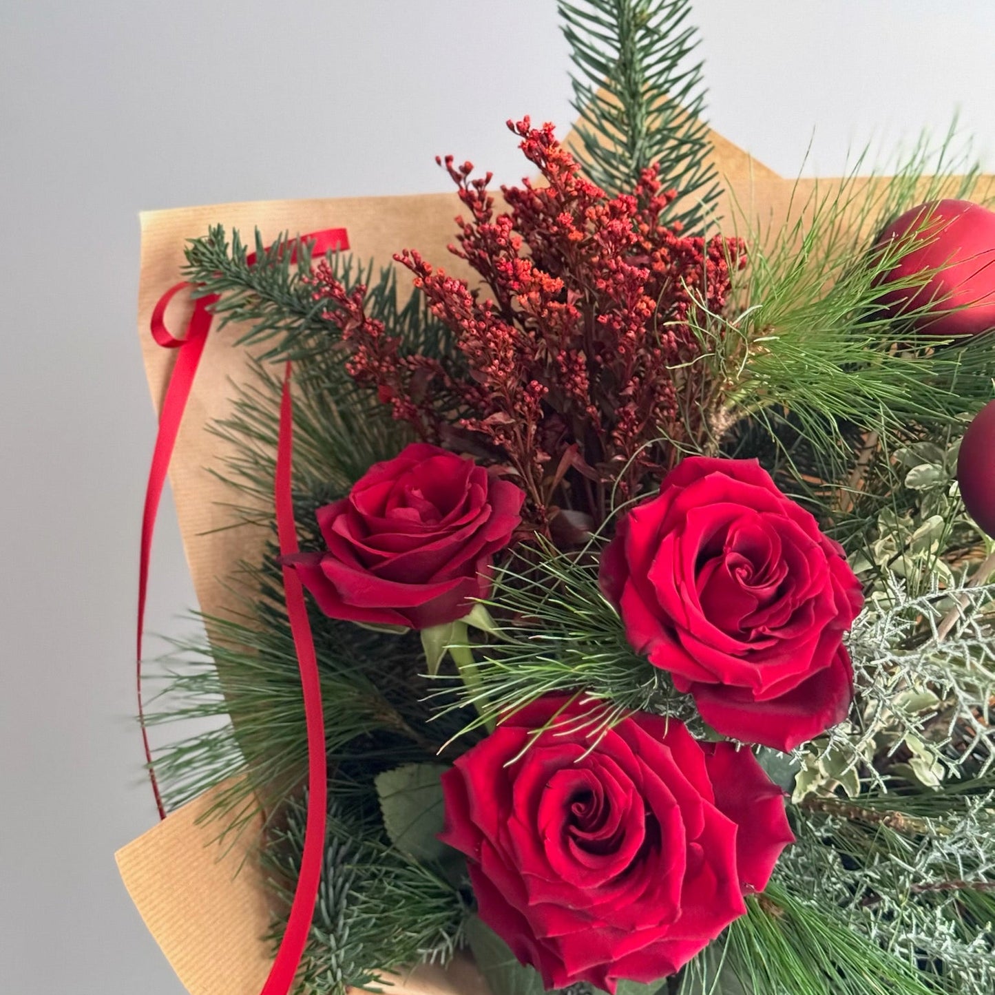Bouquet of red roses with greenery and a red ribbon on a light gray background