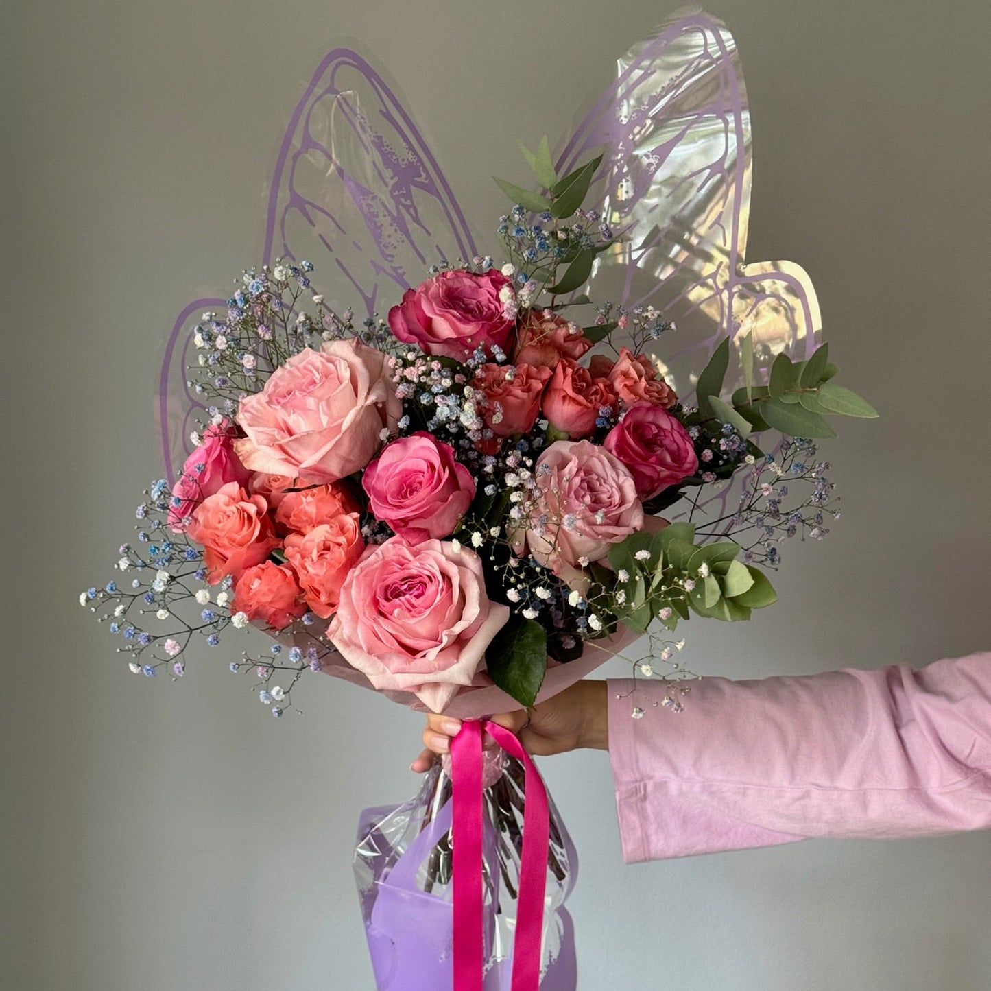 Bouquet of pink and red roses with fairy wings and a pink ribbon on a neutral background