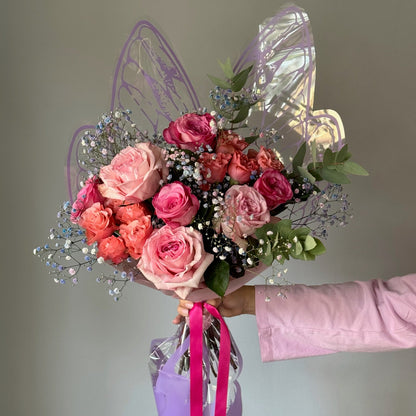 Bouquet of pink and red roses with fairy wings and a pink ribbon on a neutral background