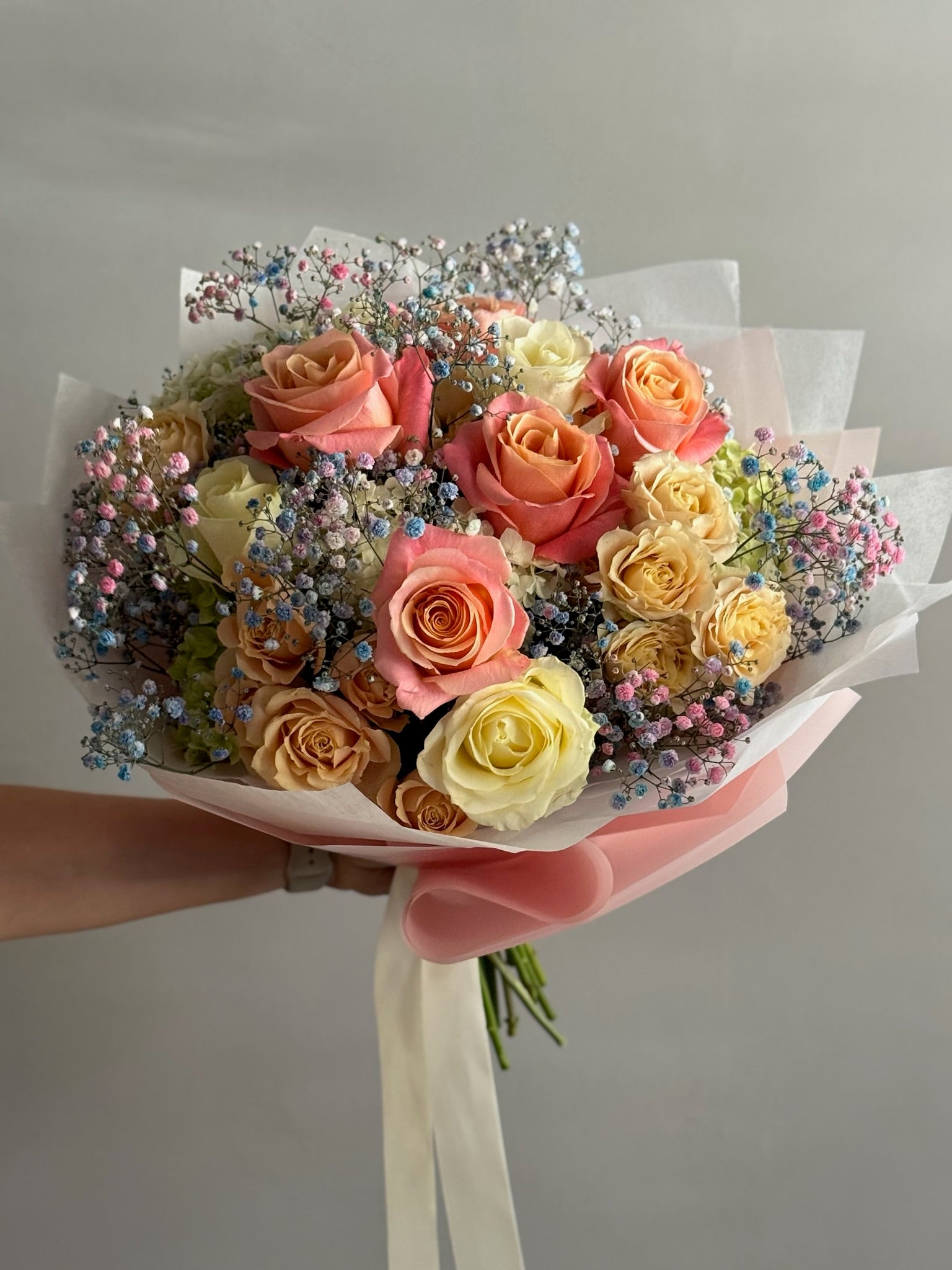 Bouquet of multicolored roses with decorative elements held by a person against a neutral background