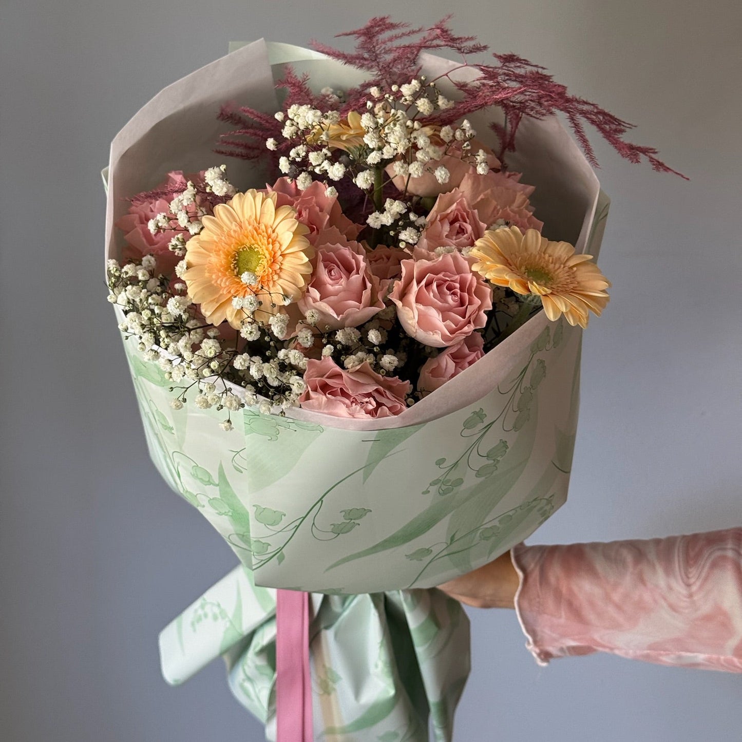 Bouquet of flowers wrapped in paper with a pink ribbon against a neutral background