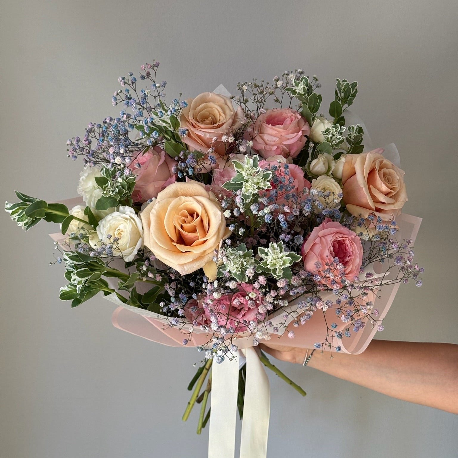 Bouquet of pastel-colored flowers held against a neutral background