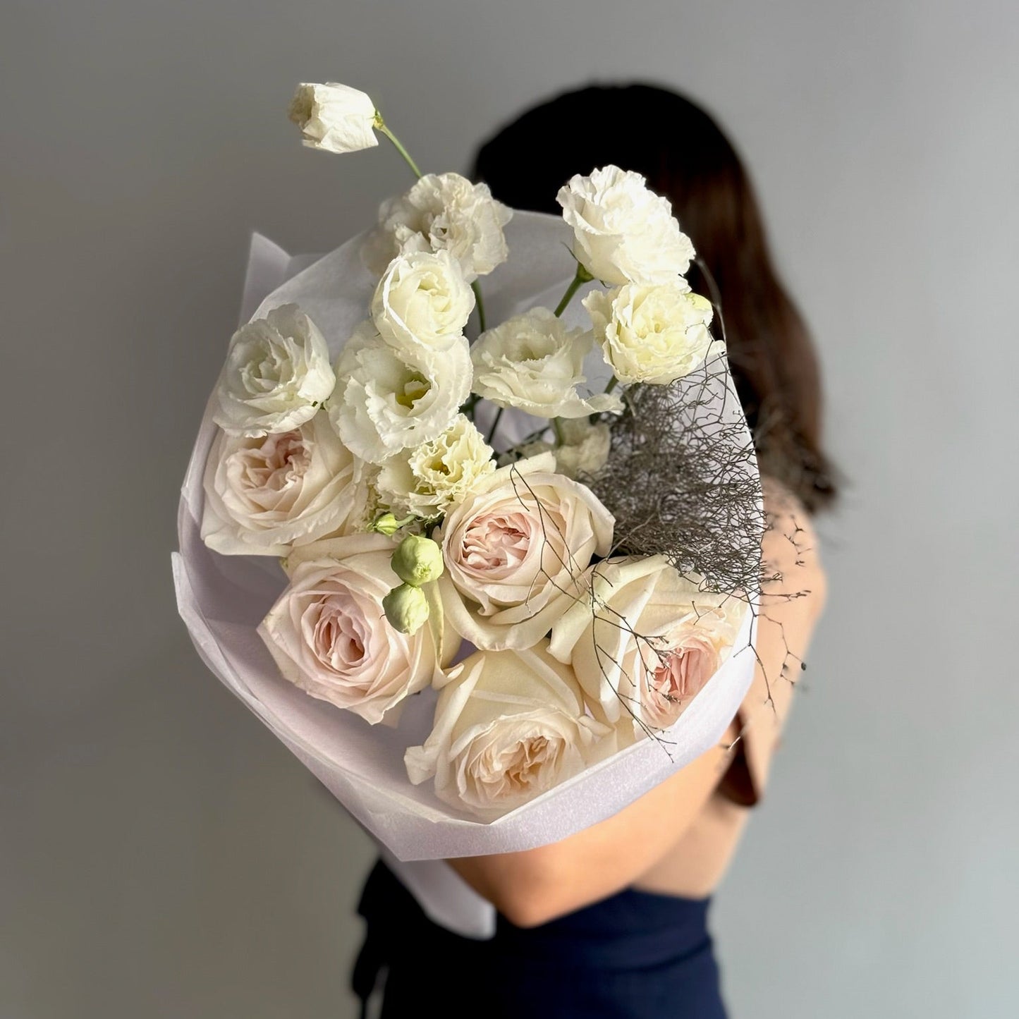 Bouquet of white and pink roses held by a person against a gray background