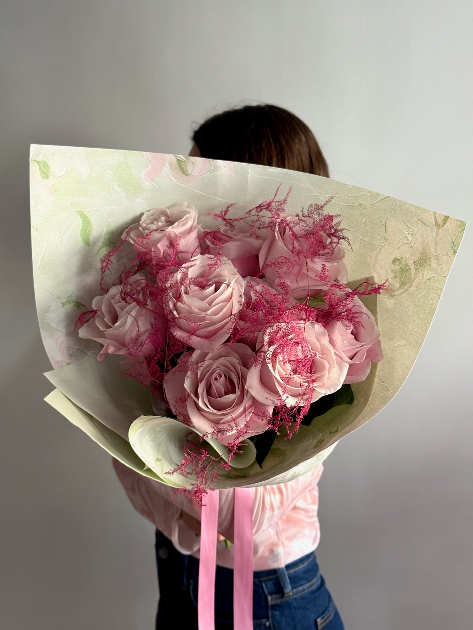 Person holding a bouquet of pink roses wrapped in paper against a plain background