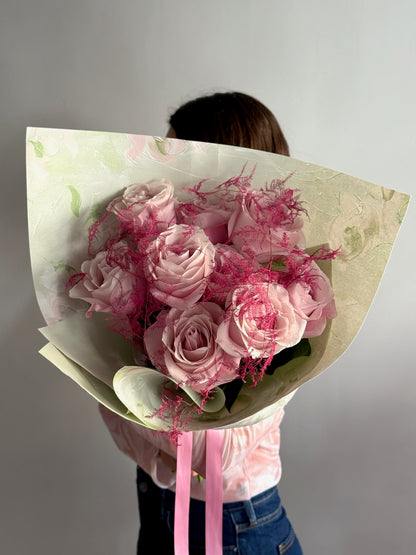 Person holding a bouquet of pink roses wrapped in paper against a plain background