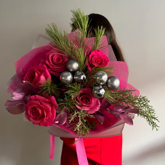 Bouquet of pink roses with greenery and silver ornaments held by a person wearing a red outfit.