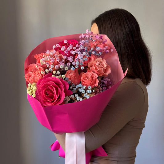 Person holding a large bouquet of flowers wrapped in pink paper against a neutral background