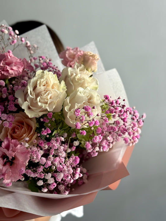 Bouquet of pink and white flowers held by a person against a neutral background