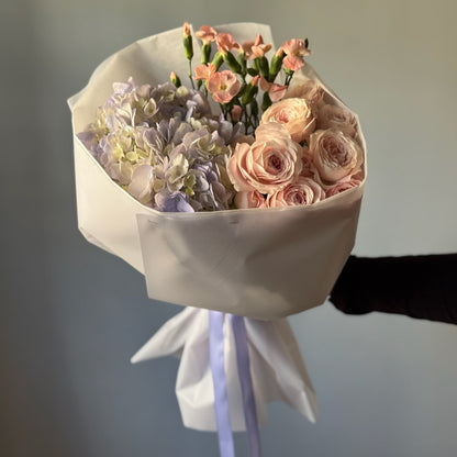 Bouquet of flowers wrapped in white paper with a blue ribbon against a neutral background