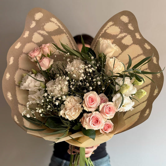 Bouquet of flowers wrapped in brown paper with a person holding it against a neutral background